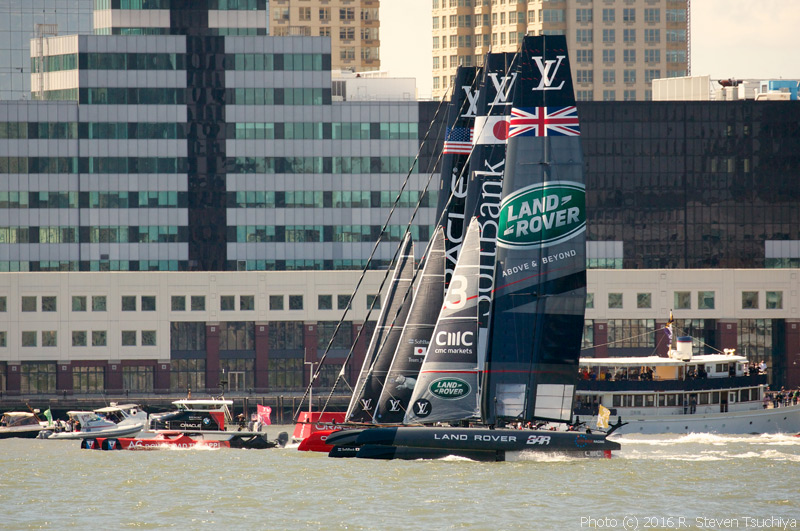 Oracle Team USA, Softbank Team Japan, and Land Rover BAR head down the Hudson River.  The red and black catamaran powerboat keeping pace with them, at left, is the on-course television camera boat.